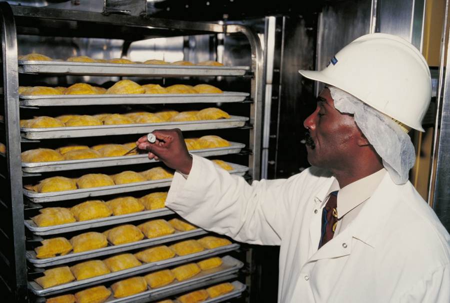 A food plant inspector in a hairnet and white coat checking trays of pastries