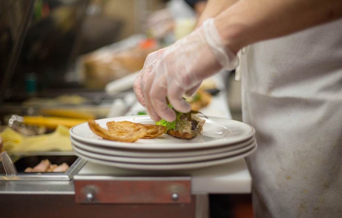A cook in disposable gloves plating food on the pass